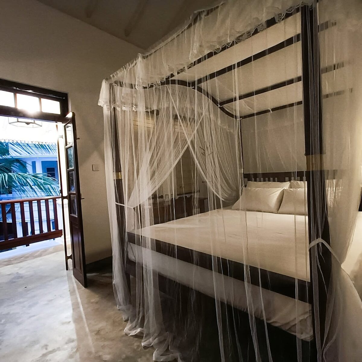 Four-poster canopy bed with white netting and balcony doors
